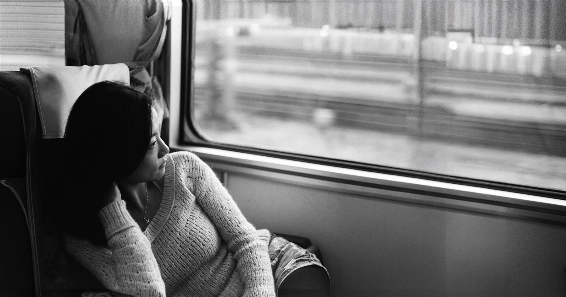 A woman sitting on a train, looking down at her phone.